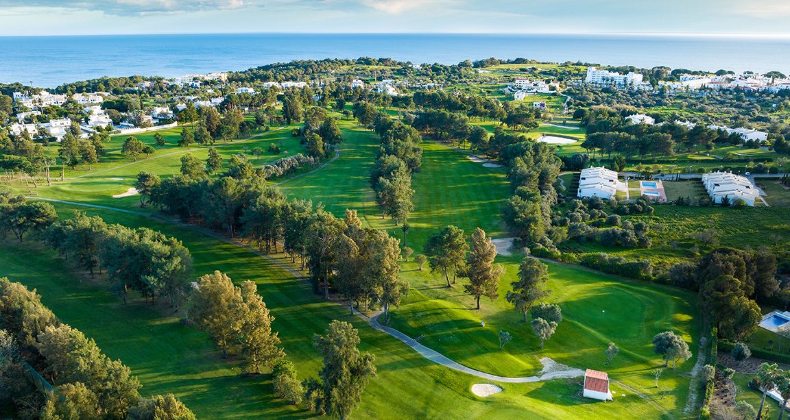 Golfbana med träd, fairways och bunkrar nära havet